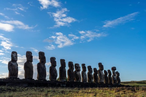 Row of fifteen Moai statues on the Ahu Tongariki stone platform against blue sky with clouds, Rapa