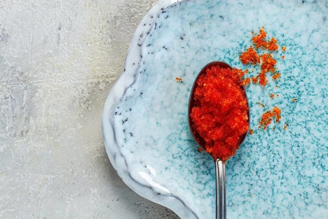 A spoon with orange flying fish caviar, Tobiko, on a light blue plate, caviar for rolls and sushi,