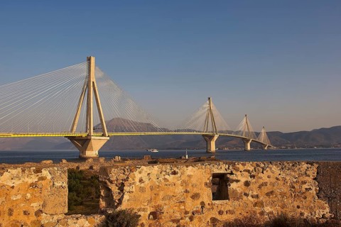 Wide view of a modern bridge that stretches majestically across the Gulf of Corinth, with ruins in