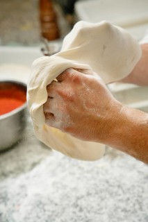 Cropped unrecognizable person skillfully prepares pizza by stretching and shaping the dough in a