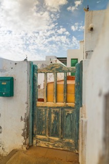 An old, turquoise wooden gate stands open, revealing a peek of a typical home in Lanzarote, Canary