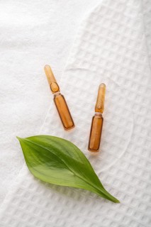 Two brown cosmetic ampoules with anti-aging serum arranged on a textured white towel, accented by a