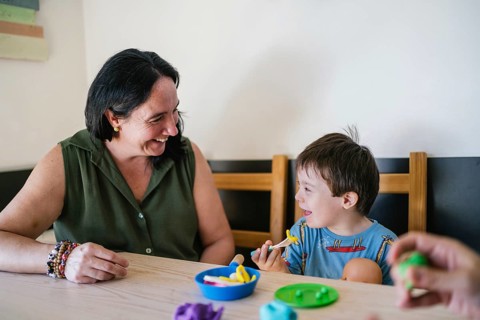 Joyful moment of a mother and her son with Down syndrome playing with pretend food at a table. They
