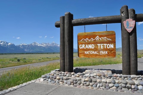 Wooden sign of Grand Teton National Park against mountain backdrop on a sunny day, Grand Teton