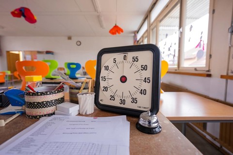 In a light-flooded room, there is a timer and a table bell on a desk, homework supervision,