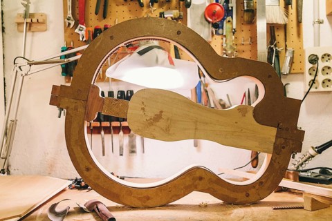 A detailed view of a bass guitar in progress at a luthier's workshop, showcasing tools and