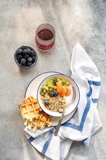 A healthy breakfast setup featuring a bowl of granola, fresh fruit, waffles, and a glass of berry