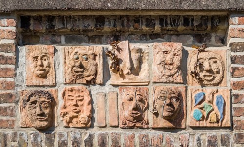 Artistic installation with mask and facial reliefs made of terracotta, in a historic brick wall,