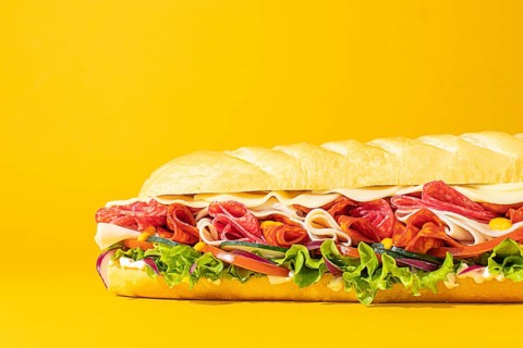Close-up of a stacked deli sandwich, styled on a vibrant monochrome backdrop, with frontal lighting