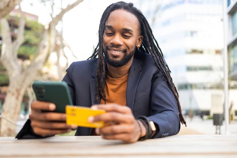 A cuban businessman with long hair smiles as he looks at his smartphone, holding a credit card. He