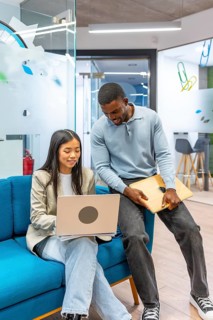 Two young professionals are working together in a modern coworking space, using a laptop and