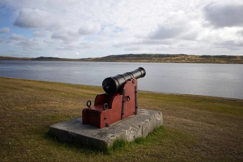 An old, weathered cannon sits on a massive concrete block overlooking the calm waters of the
