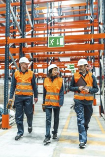 Warehouse workers wearing safety vests and hard hats are walking through a large distribution
