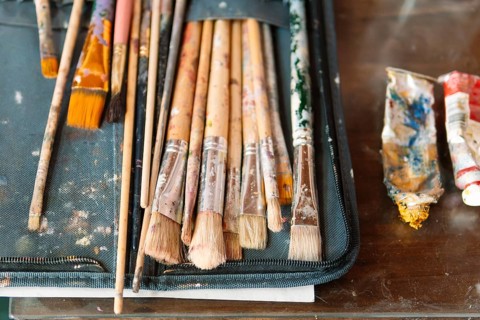 A collection of well-used paintbrushes with dried paint rests in a fabric case, alongside squeezed