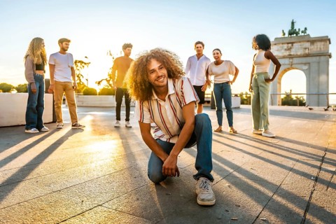 Man with curly hair and casual clothes keeling looking at camera and smiling next to multi-ethnic