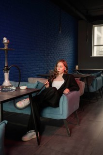 A woman relaxes in a cozy hookah lounge, enjoying the atmosphere. The modern decor features a blue