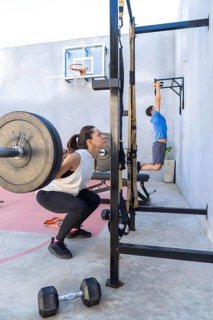 Woman is doing squats with a barbell while a man performs pull-ups in an outdoor gym, showcasing