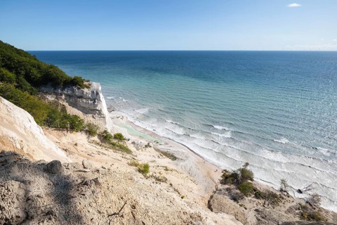 White chalk cliffs in August. People on the beach and by a small lagoon. Milky Baltic Sea under a