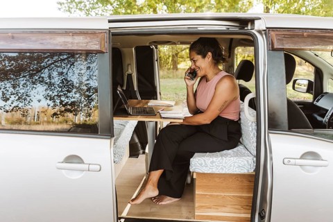 A woman works remotely from her van, surrounded by the vibrant colors of autumn in New Zealand. She