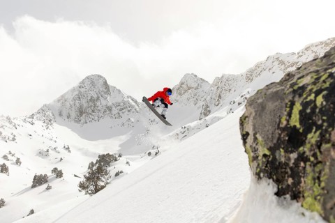A snowboarder in vibrant gear performs a daring jump in the backcountry, surrounded by majestic