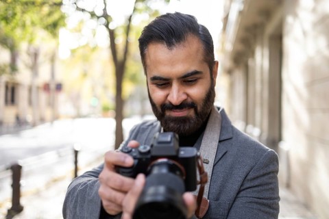 Indian male photographer smiles while focusing on his camera, dressed in elegant winter apparel on