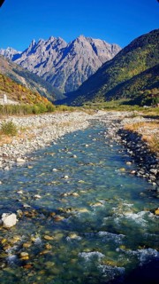 A clear river snakes through a rocky valley surrounded by high, forested mountains under clear