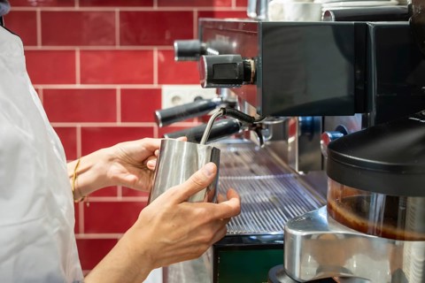 Barista hands holding a stainless steel pitcher, steaming milk using an espresso machine's wand,