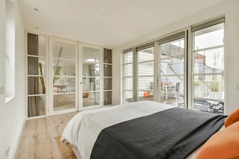 Bright modern bedroom featuring large glass doors, minimalist design, and contemporary furnishings,