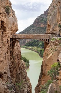 A wooden bridge hovers over a river, surrounded by dramatic cliffs on the Caminito del Rey hiking