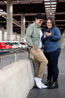 A joyful lesbian curvy couple shares a fun moment while looking at a smartphone. They are standing