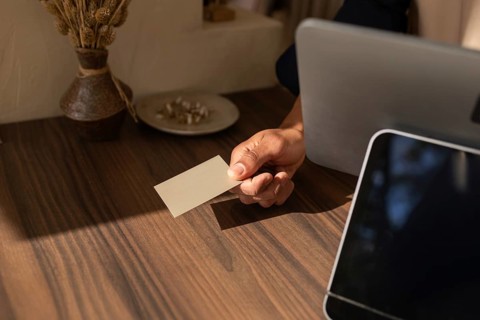 A customer hands a card over the checkout counter in a stylish bag store, with a vase and laptop