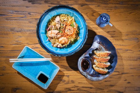 Wok noodles with shrimps and chicken, gyoza dumplings and soy sauce served on a wooden table,