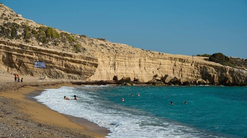 Beach with bathers next to rocky coast and clear blue water under a sunny sky, Cape Fourni, Fourni