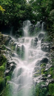 A breathtaking view of a layered waterfall cascading over jagged rocks through a lush, verdant