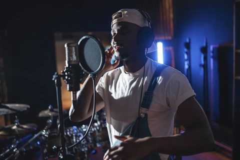 Young black artist wearing headphones and singing into microphone, recording a new album in