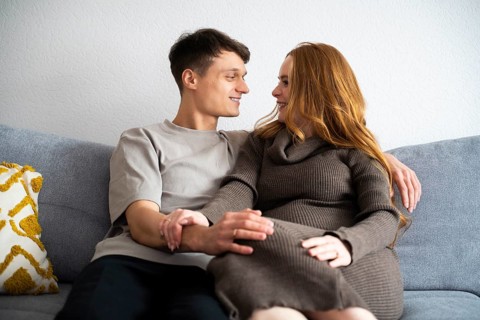 A young couple expecting a baby sits together on a comfy couch, symbolizing love and anticipation.