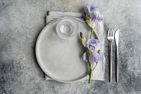 Top view of an elegant table setting featuring a concrete textured plate, clear glass, silverware,