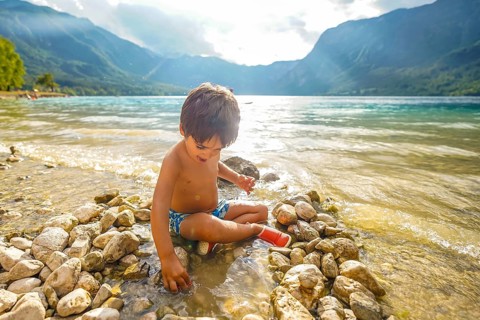 Young boy enjoying summer holidays, playing on the rocky shore of lake bohinj in slovenia,