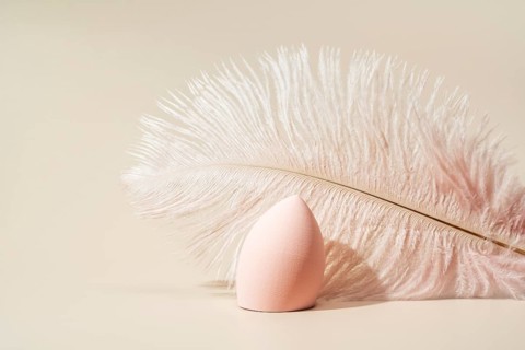 A soft pink cosmetic sponge elegantly paired with a delicate feather on a beige background The
