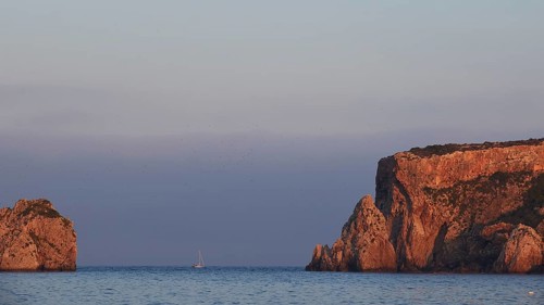 Cliff landscape with a sailboat off the coast at sunrise, morning light, islet of Tsichli Babas,