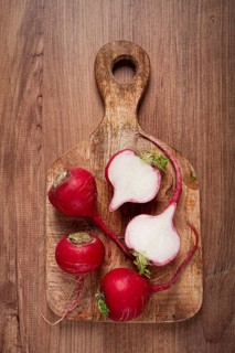 A wooden cutting board features freshly picked radishes, showcasing their vibrant red skins
