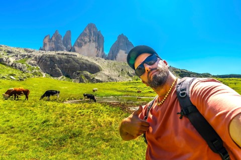 Bearded tourist taking a selfie while hiking in the tre cime di lavaredo natural park with cows