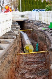 Open trench with a large district heating pipe and white barriers on a road