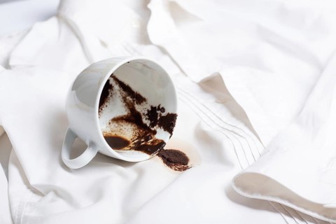 A white cup with the remains of coffee, spilled, lies on a white shirt, there are no people, a soft