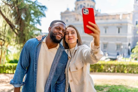Frontal view of a happy multi-ethnic couple embraced taking selfie in city viewpoint