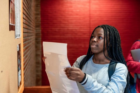 Young student consulting a bulletin board in a university hallway, focusing on important