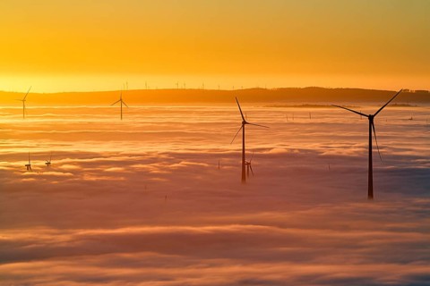 Wind turbines rising from cloud cover, wind farm, silhouettes at sunset, dense sea of fog in the