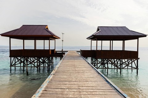 Top view of two traditional overwater gazebos connected by a wooden pathway in the pristine Raja