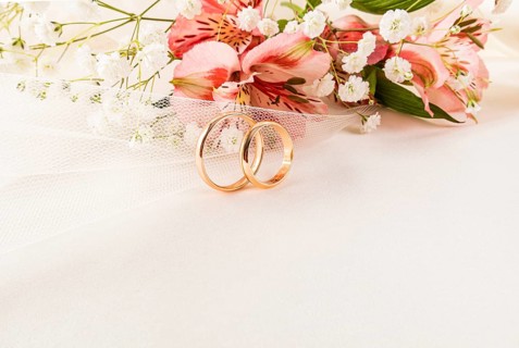 Elegant composition of two gold wedding rings surrounded by delicate pink and white flowers on a