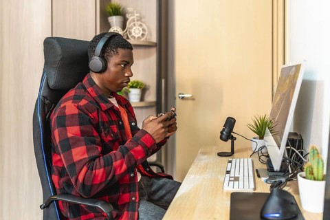 Young man concentrating on a video game, using a controller and headset while sitting at his desk